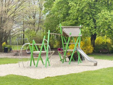 Villach, Avusturya - 17 Nisan 2025: Çocuklar için kaydırak ve tırmanma yapısına sahip canlı yeşil bir parka kurulmuş renkli oyun alanı ekipmanları