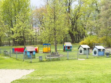 Villach, Avusturya - 17 Nisan 2025: Yeşillik bir parkta köpek evleri ve oyuncakların yer aldığı renkli evcil hayvan oyun alanı, evcil hayvanlar için açık hava aktivitelerini teşvik ediyor