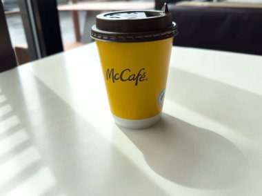 Villach, Avusturya - 17 Nisan 2025: Güneş ışığıyla aydınlatılmış bir masanın üzerindeki kahve fincanı, parlak sarı bir tasarım ve McCafe markasının yer aldığı gölgeler yaratır.