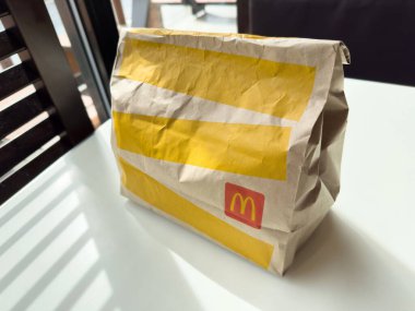 Villach, Avusturya - 17 Nisan 2025: Uygun yiyecek kültürünü temsil eden masanın üzerinde kendine özgü sarı çizgili ve logolu fast food paket paketi