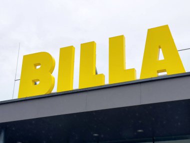 Villach, Avusturya - 17 Nisan 2025: Açık sarı BILLA mağaza tabelası modern perakende markalaşma ve alışveriş deneyimini vurgulayan bulutlu bir gökyüzüne karşı duruyor