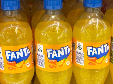 Villach, Avusturya - 17 Nisan 2025: Portakallı gazoz şişeleri düzgün bir şekilde rafa dizilmiş, parlak renkler ve ünlü Fanta içeceği markası sergilenmektedir