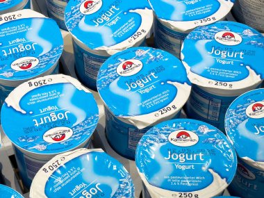 Villach, Avusturya - 17 Nisan 2025: Bir pazarda yığılmış yoğurt kapları süt ürünlerini ön plana çıkarıyor ve tüketiciler için sağlıklı seçenekleri teşvik ediyor