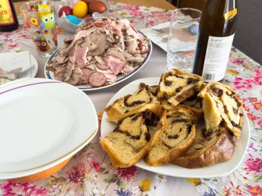 Geleneksel Paskalya yemeği, çiçekli masa örtüsünde sergilenen babka ekmeği ve soğuk pirzola dilimleri..
