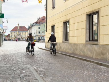 İki yetişkin bulutlu bir günde tuhaf Avrupa caddelerinde bisiklet sürüyor..