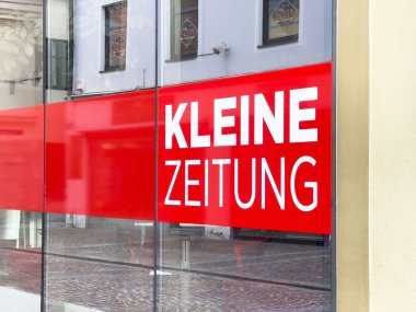 Cam binanın önündeki kırmızı pankartta Kleine Zeitung işareti var..