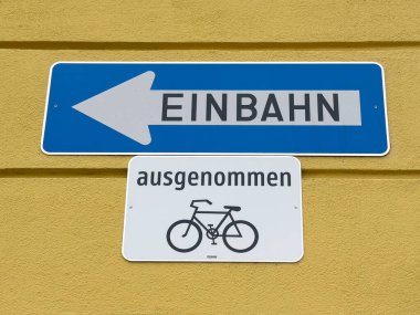 Sarı duvarda bisiklet istisnası olan tek yönlü Alman sokak tabelası.