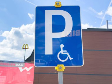 Fast food restoranının yanında mavi arka planı ve simgesi olan ulaşılabilir park yeri tabelası.