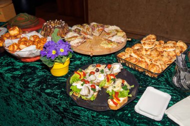 Çeşit çeşit hamur işleri ve sandviçler yeşil masa örtüsü ve mor çiçekli..