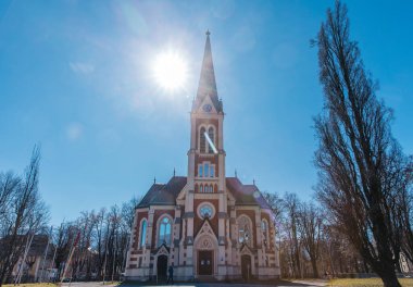 Uzun çan kulesi ve berrak mavi gökyüzü ile güneşli gotik kilise cephesi.