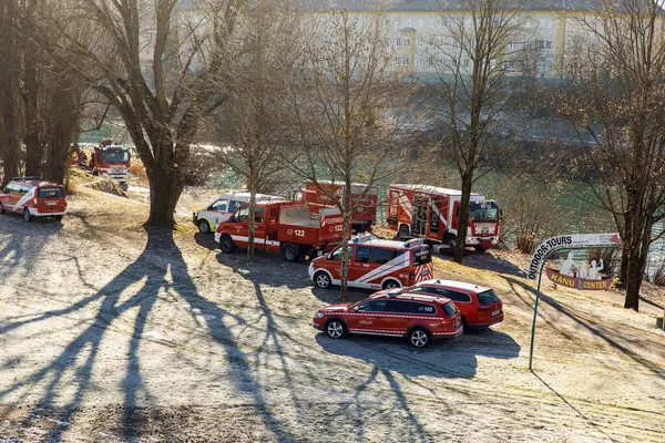 Kışın nehir kıyısında ağaçlarla çevrili acil durum araçları..