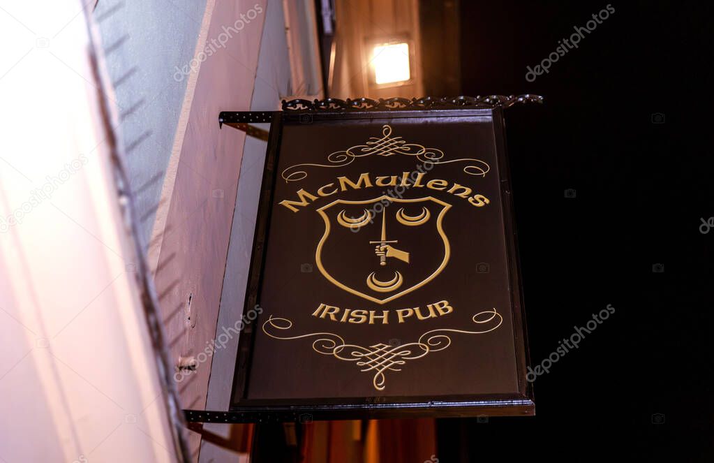 Mcmullens irish pub sign at night with decorative design and warm lighting.