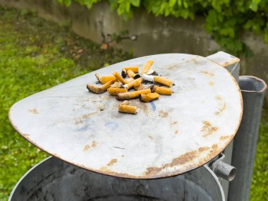 Açık hava ortamında metal çöp kapağında sigara izmaritleri..