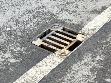 Paslı yol kenarı drenajı beyaz çizgili asfalt üzerinde.