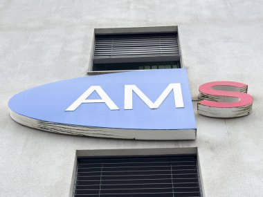 Beton duvarda mavi ve kırmızı harflerle Ams binası tabelası.