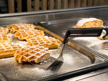 Altın waffle 'lar pudra şekeri ile mutfak tezgahında sıcak bir ızgarada.