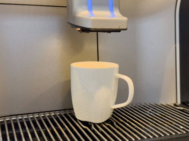 Kahve makinesi, minimalist mutfak ortamında beyaz bardağa dökülüyor..