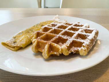 Lezzetli Belçika waffle 'ı ve beyaz tabakta pudra şekerli krep..