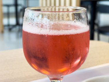 Hafif ahşap bir masada cam bir kadehte köpüklü pembe içecek..