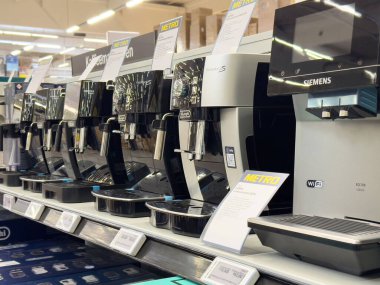 Marka etiketleri ve özellikleri olan modern kahve makineleri mağazada sergileniyor.