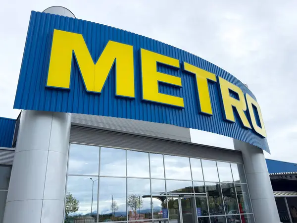 Metro mağazasının ön girişi, modern binanın dış tarafında koyu sarı bir tabela var..