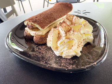 Krem şantili tiramisu tatlısı ve siyah tabakta kakao..