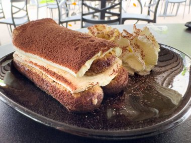 Açık kafe ortamında siyah tabakta krem şantili nefis tiramisu..