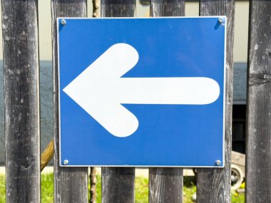 Ahşap çit arka planında mavi sol ok trafik işareti.