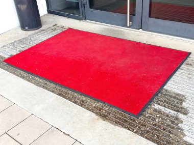 Siyah kapılı ve fayanslı binaların girişinde parlak kırmızı bir hoş geldin paspası..