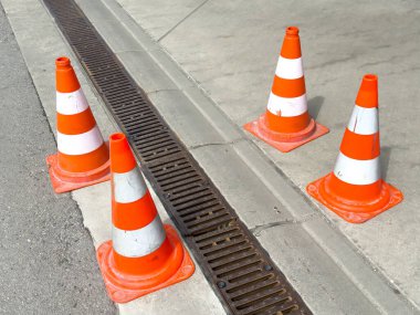 Dört turuncu trafik konisi kaldırımın kenarına dizilmiş..