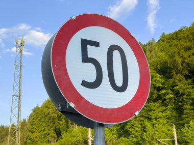 Bereketli yeşil orman arka planına karşı saatte 50 km hız sınırı işareti.
