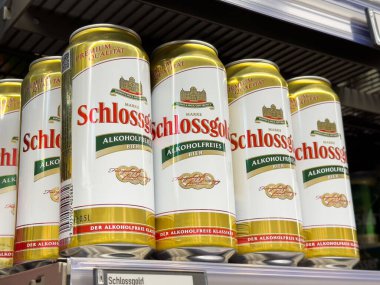 Villach, Avusturya - Mayıs 06, 2025: Schlossgold 'dan alkolsüz bira kutuları, çekici tasarımları ve markalarını ön plana çıkaran bir süpermarket rafında güzelce düzenlenmiştir.
