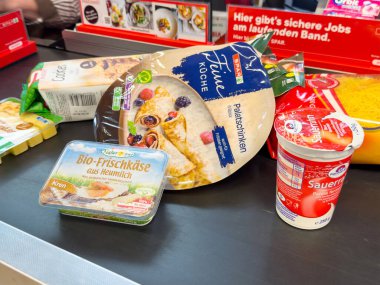 Villach, Avusturya - 06 Mayıs 2025: Taze peynir, yoğurt ve krep gibi çeşitli market ürünleri bir süpermarket kasasında düzenlenir