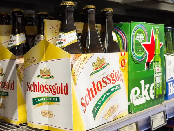 Villach, Avusturya - 06 Mayıs 2025: Schlossgold alkolsüz bira şişelerinin arka planda renkli bira markalarıyla süpermarket raflarında sergilenmesi