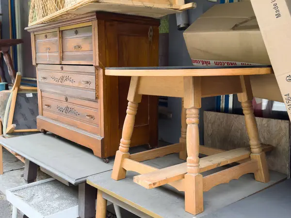 Villach, Avusturya - 06 Mayıs 2025: Bir sandık çekmece ve kırsal masa içeren eski ahşap mobilyalar, çeşitli eşyaların bulunduğu bir depoda düzenlenmiştir.