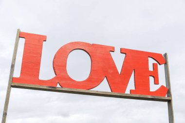 Ahşap çerçevedeki kırmızı aşk işareti bulutlu gökyüzü arkaplanına karşı.