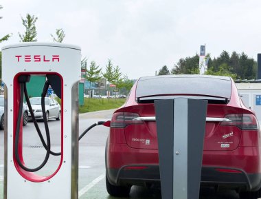 Kırmızı Tesla X modeli bulutlu gökyüzü ile şehir merkezinde şarj oluyor.