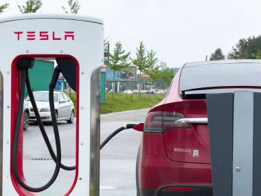 Şehir merkezindeki elektrik santralinde kırmızı Tesla SUv şarj ediliyor.