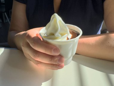 Kadın elinde vanilyalı dondurma bardağıyla güneşli kafede.