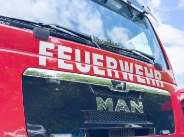 Alman kırmızı itfaiye aracının önünde gökyüzünü yansıtan işaret levhası var..