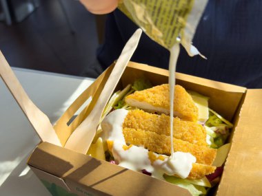 Ekmekli tavuklu taze salata ve karton bir kutuda sos..