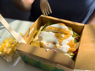 Sos soslu taze tavuk salatası kutusu ve masa üzerinde güneş ışığında ahşap çatal..