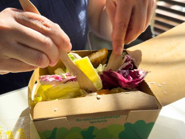 Güneşli bir günde ahşap çatallı ve kutulu taze salatanın tadını çıkaran bir insan..