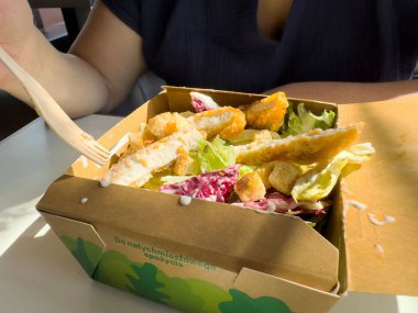 Taze tavuk sezar salatasının tadını çıkaran bir kadın. Yanında da ekosistem ambalajlı kızarmış ekmek..