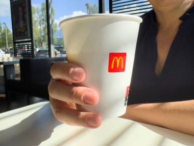 Yetişkin beyaz kadın McDonald 'ın kahve fincanını güneş ışığında fast food restoranında tutuyor..