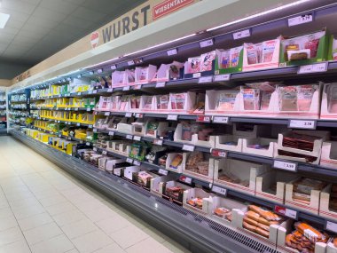 Raflarda çeşitli paketlenmiş et ve süt ürünleri bulunan geniş bir süpermarket koridoru.