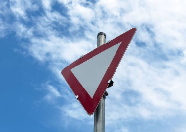 Mavi gökyüzüne karşı kırmızı kenarı olan üçgen verim trafik işareti.