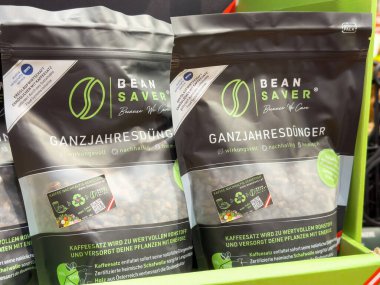 Rafta geri dönüşüm sembolleri ve Almanca metin içeren fasulye koruyucusu gübre torbaları var..