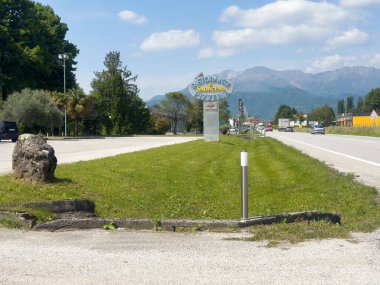 Mavi gökyüzünün altındaki dağlık araziye giden yol kenarında pizzacı tabelası var..