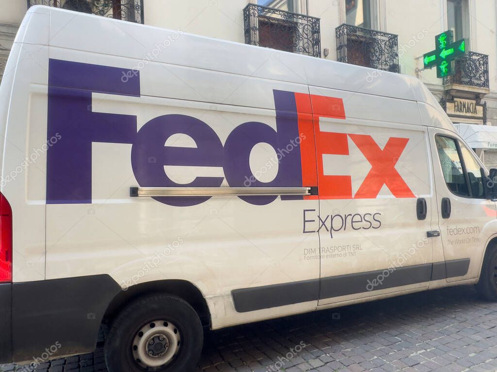Fedex express delivery van parked on city street with pharmacy sign and cobblestone road.